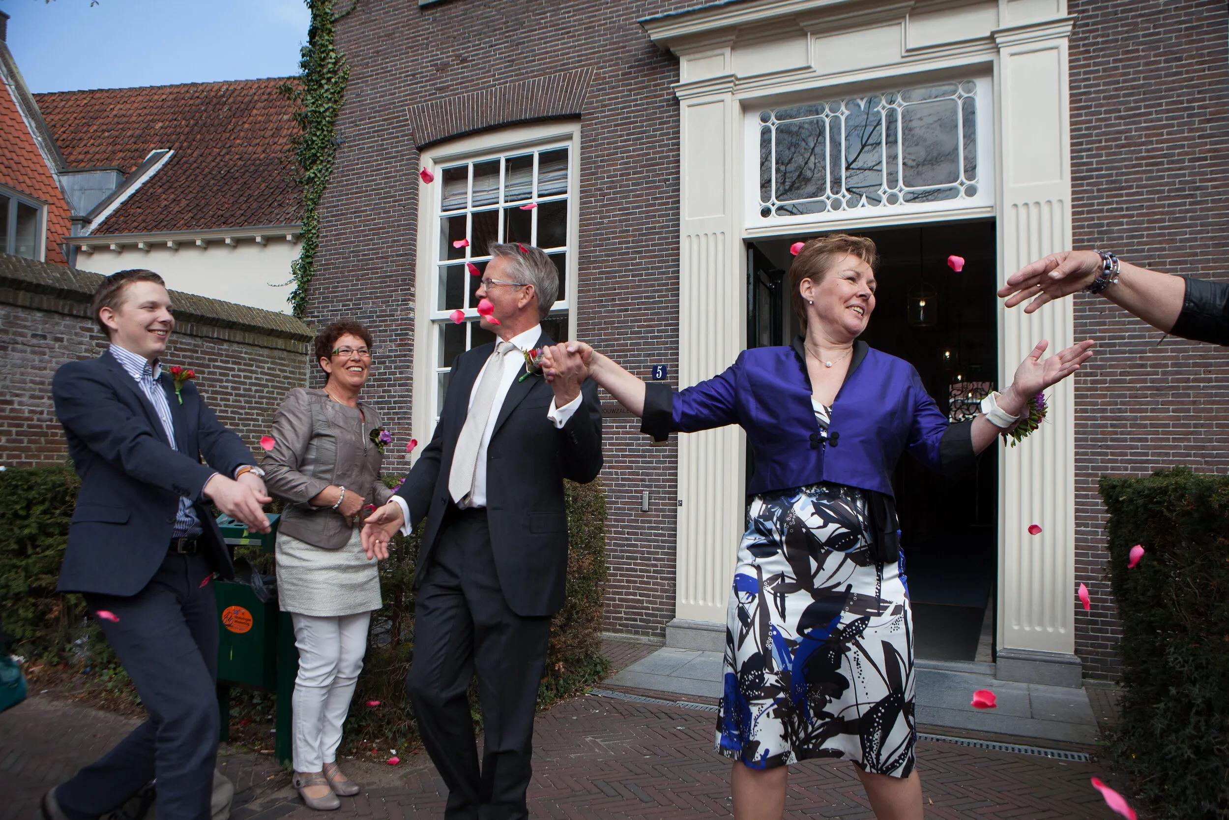 Carolien en Jelle komen hand in hand naar buiten na hun ceremonie in Amersfoort, terwijl de gasten rozenblaadjes gooien