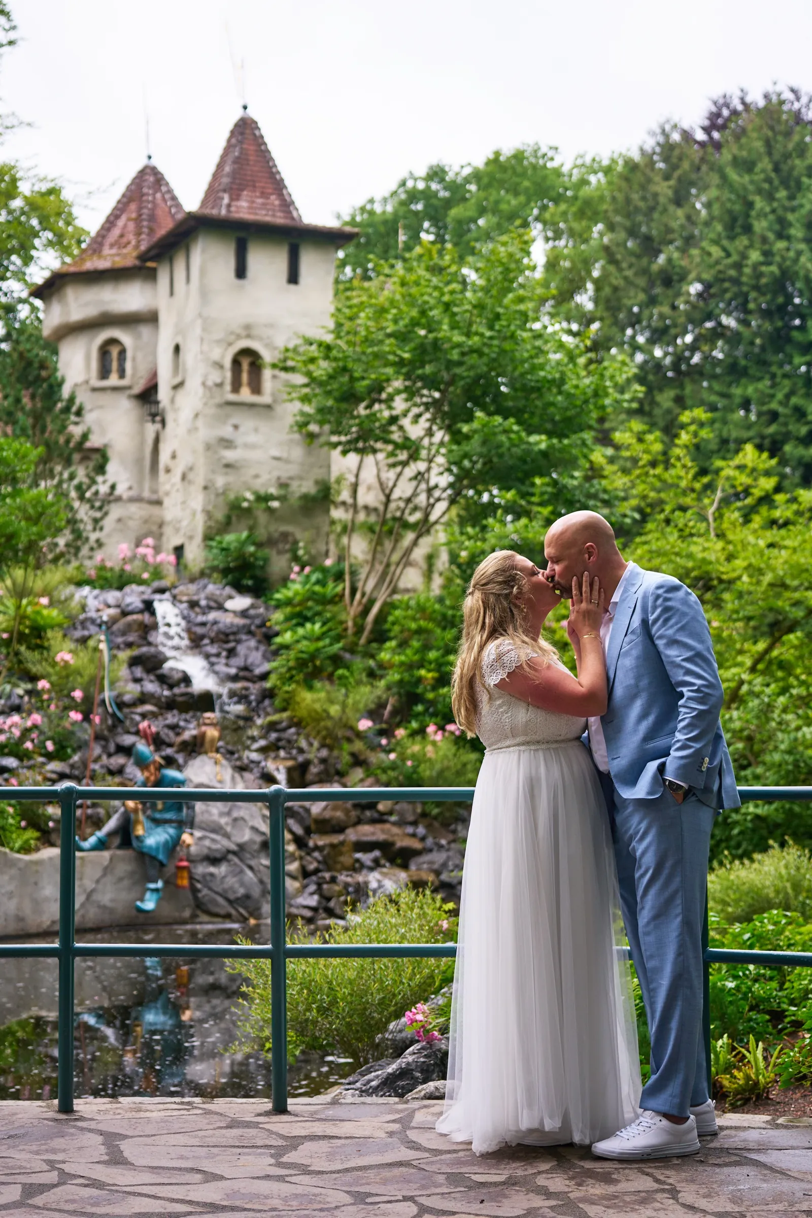 Annemarie en Jan kussen bij een waterval in de Efteling, met een torentje erachter