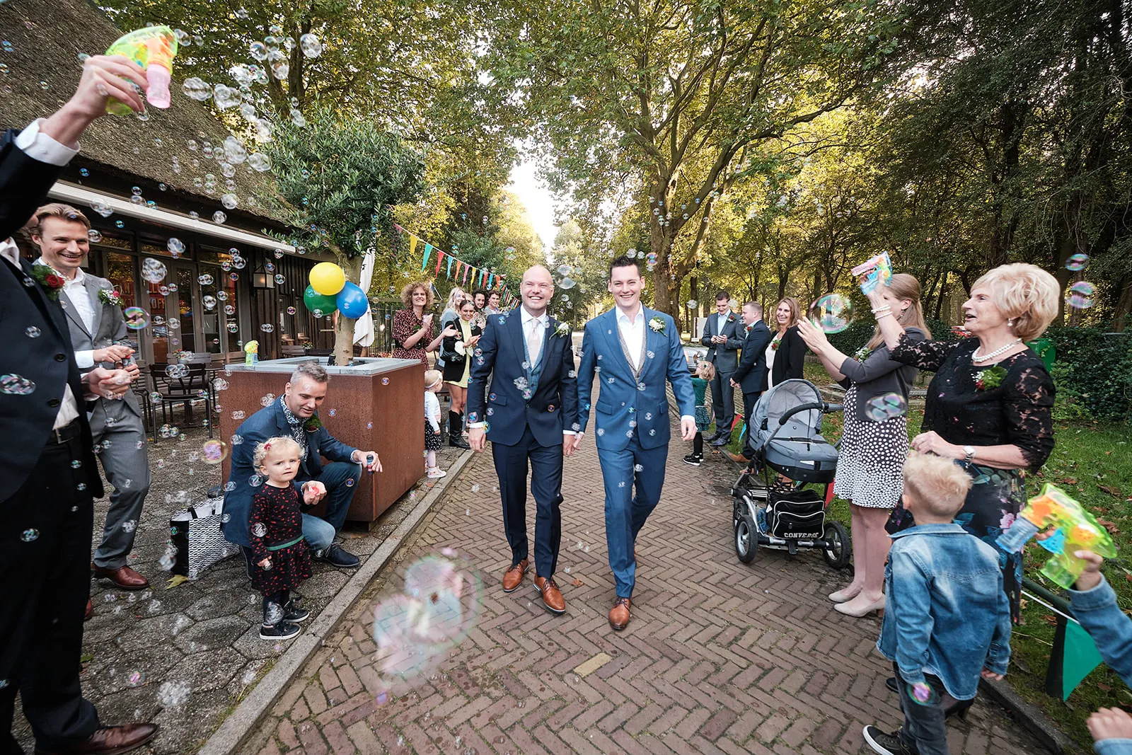 Matthijs en Jeroen lopen hand in hand naar De Schaapskooi, terwijl de gasten bellen blazen