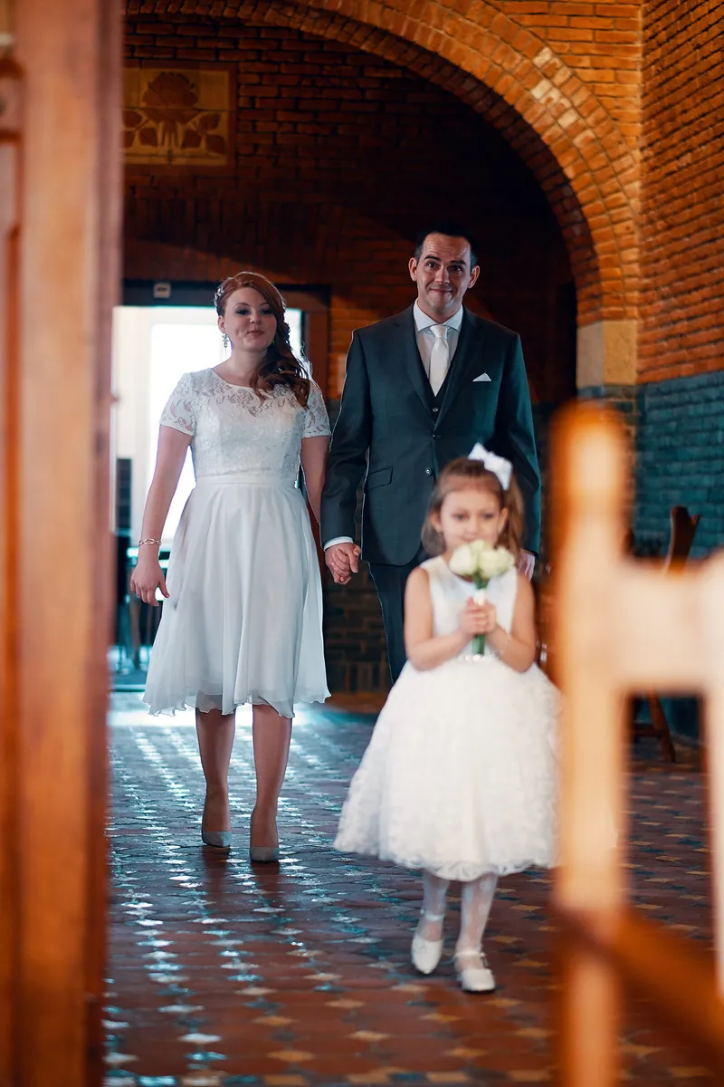 Naomi en Maurice lopen de trouwzaal binnen, het bloemenmeisje loopt voorop