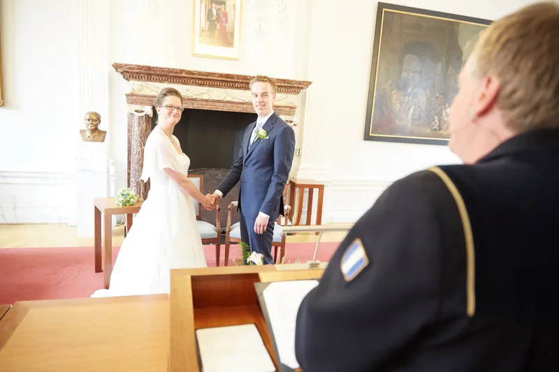 De ambtenaar met het bruidspaar voor de schouw