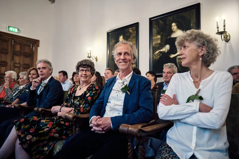 Gasten lachen tijdens de ceremonie onder de schilderijen in de trouwzaal