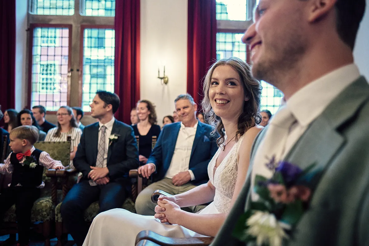 Renske en Tijmen kijken elkaar aan tijdens de ceremonie, met de glas-in-loodramen erachter