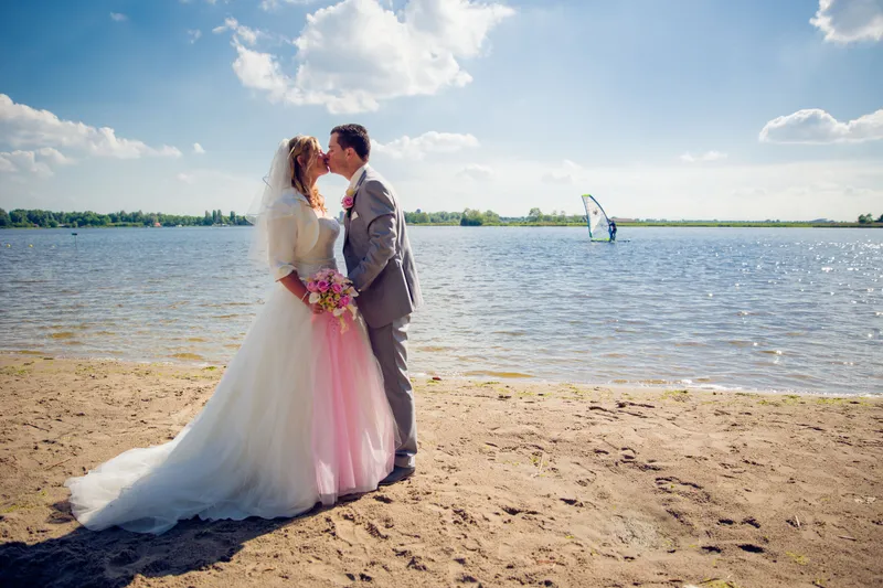 Jennifer en Brian kussen op het strand, de sluier waait mee