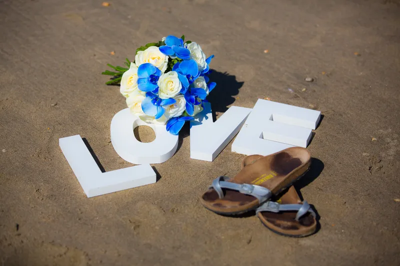 Witte LOVE-letters met het boeket en slippers in het zand