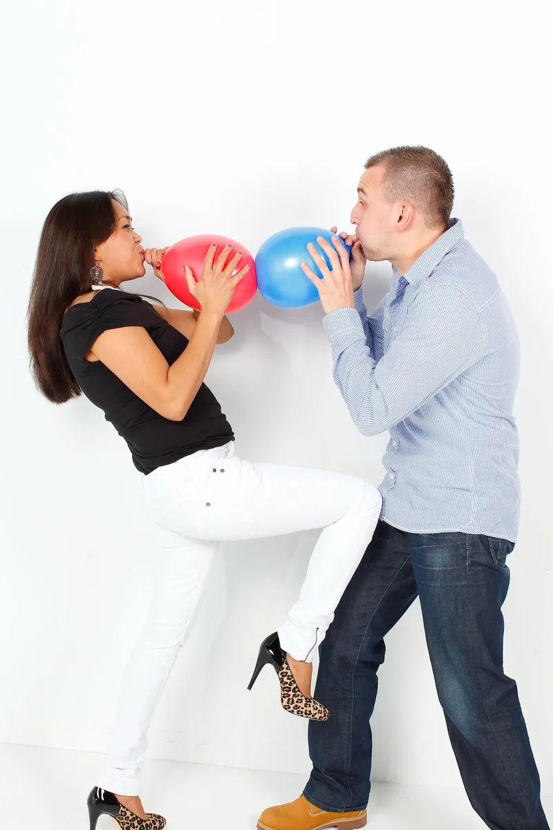 Stel blaast lachend rode en blauwe ballonnen op in de witte studio