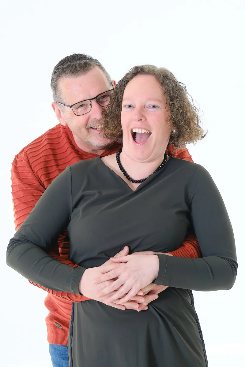 Lachend stel, hij slaat van achteren zijn armen om haar heen, tegen een witte achtergrond