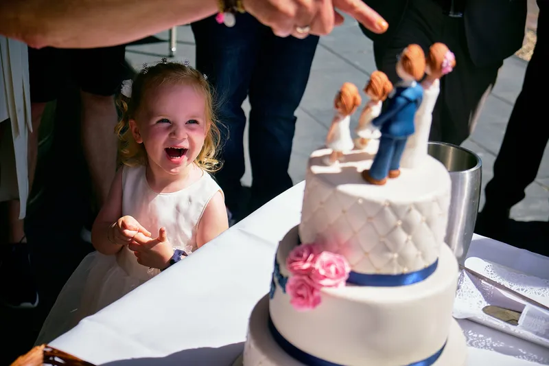 Een meisje lacht naar de bruidstaart met de poppetjes van het bruidspaar
