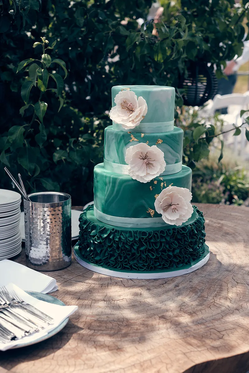 Een groene bruidstaart met witte suikerbloemen in de tuin