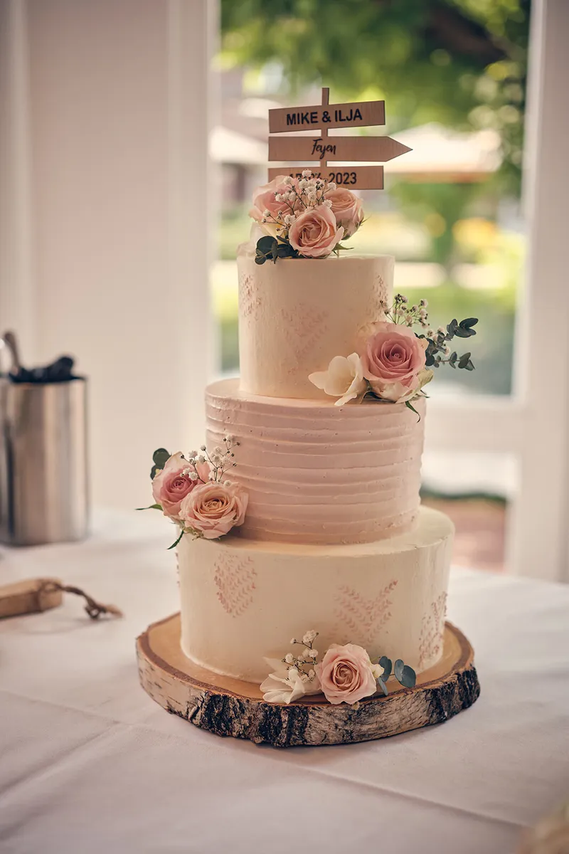Een witte bruidstaart met roze rozen op een houten boomschijf