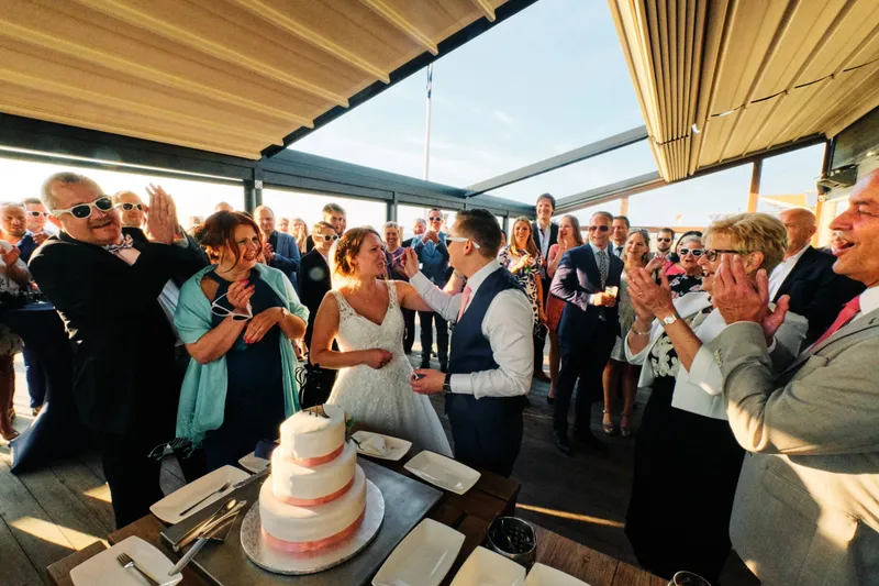 Bruidspaar snijdt de taart aan op een zonnig terras, omringd door gasten