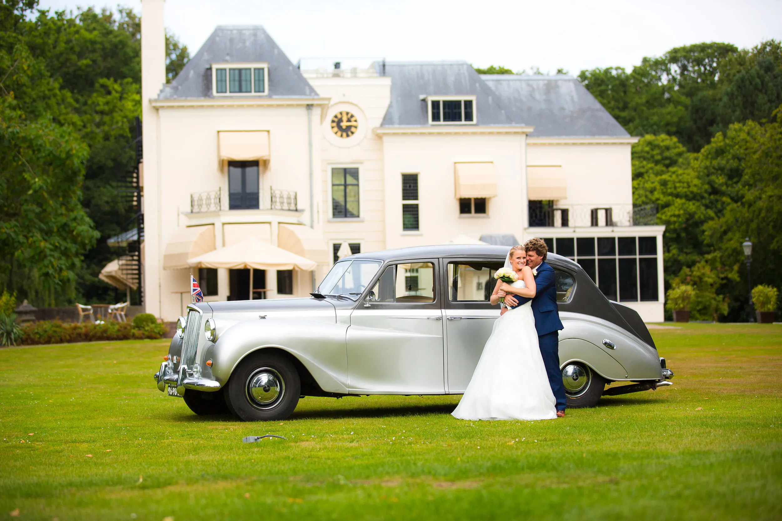 Liselotte en Matthijs bij de zilveren Austin Princess op het gazon voor Te Werve