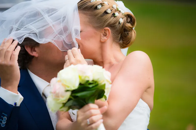 Liselotte en Matthijs kussen achter de sluier en het boeket