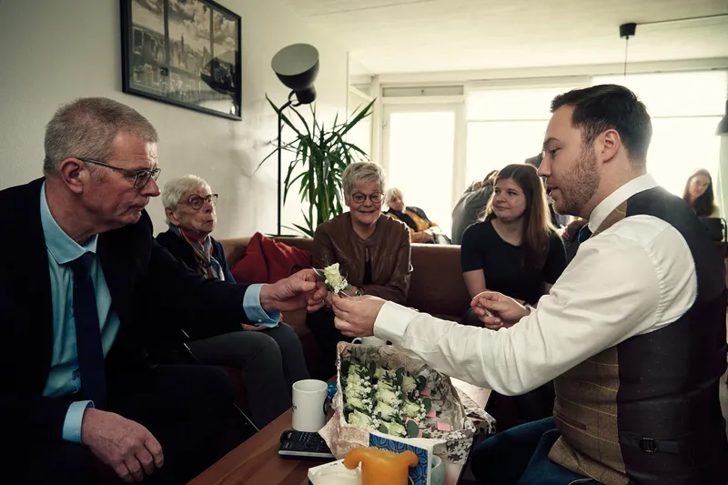 Een van de mannen speldt een corsage op bij een gast in de woonkamer