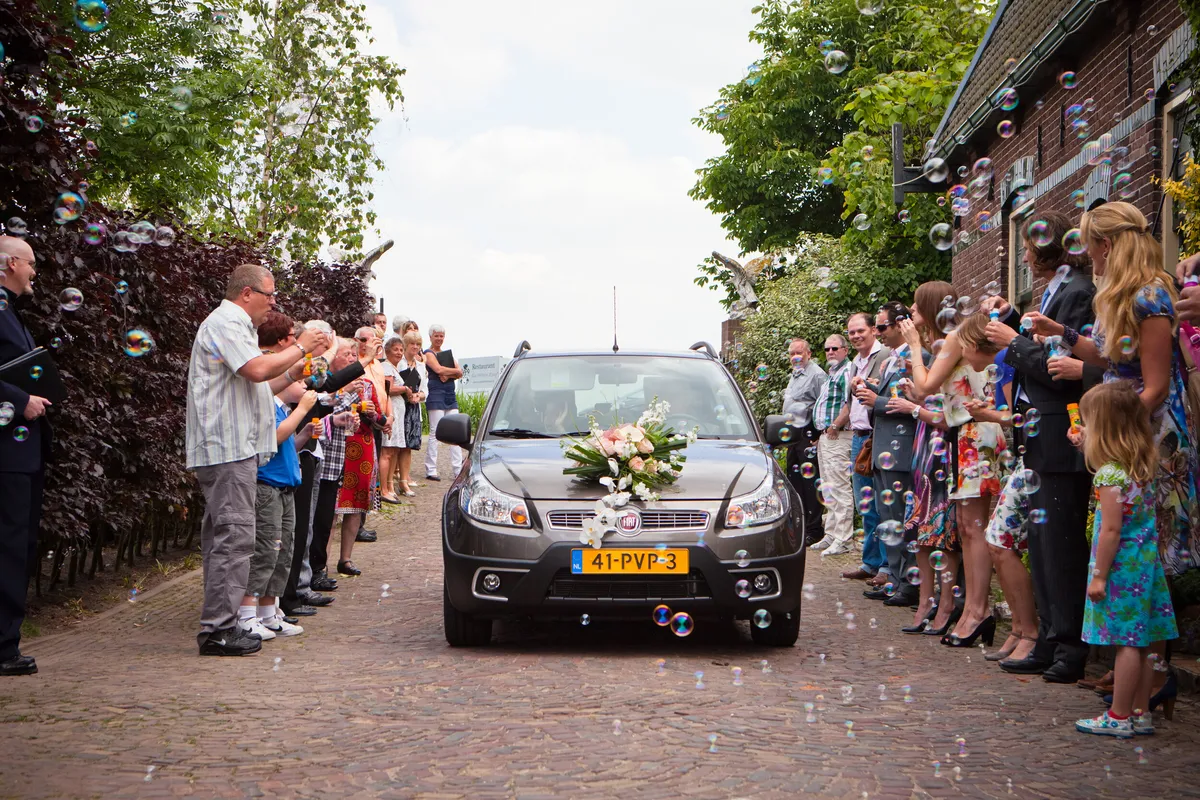 De trouwauto rijdt door een haag van buren en familie
