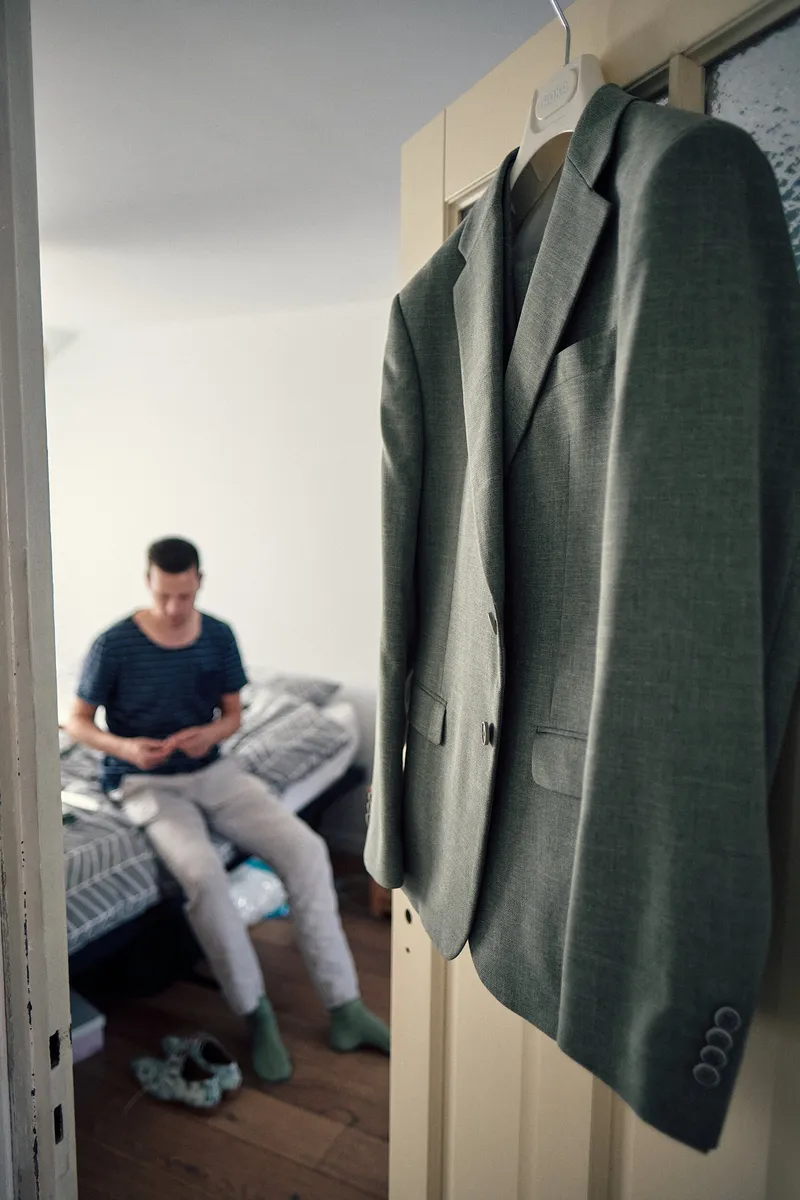 Het groene pak van Tijmen hangt aan de deur, terwijl hij op bed zit