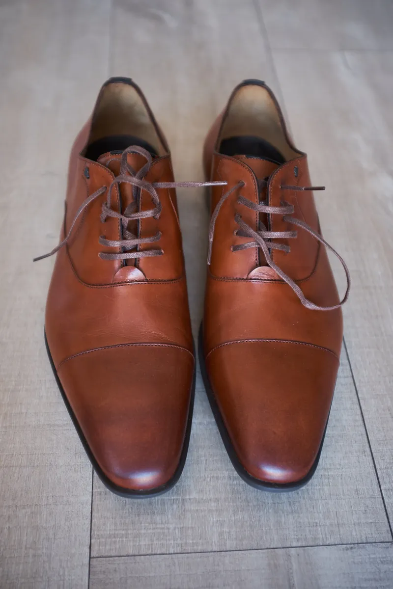 De bruine leren schoenen van Richard op de houten vloer