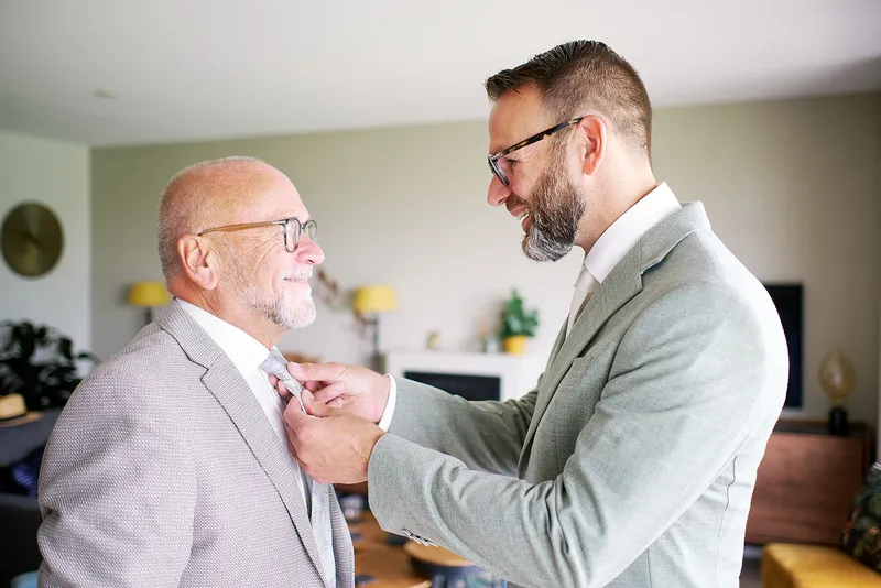 Een oudere man helpt Sander met zijn das in de woonkamer