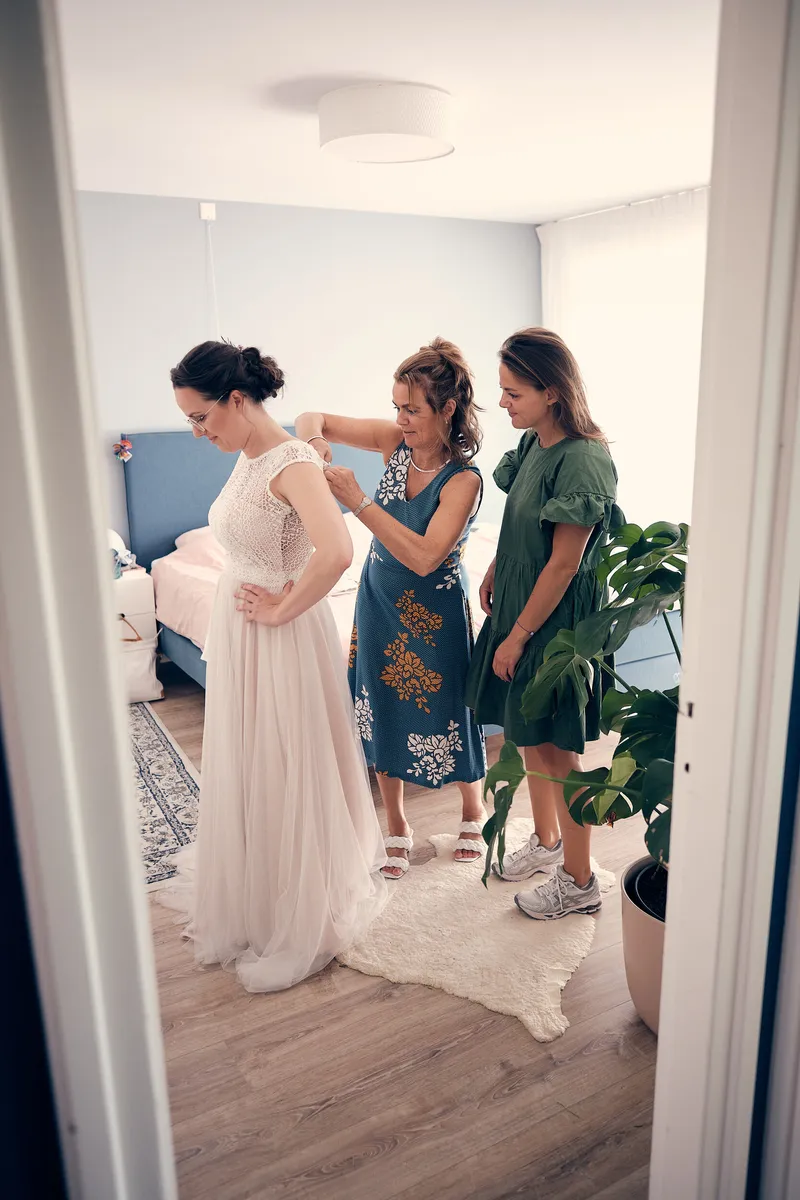 Twee vrouwen maken de trouwjurk van Evelien dicht in de slaapkamer