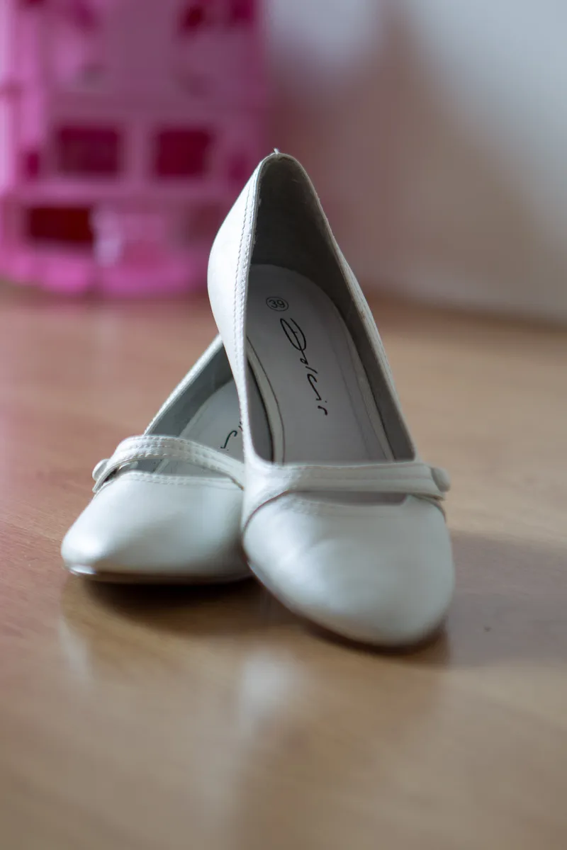 De witte bruidsschoenen van Anouk op de houten vloer