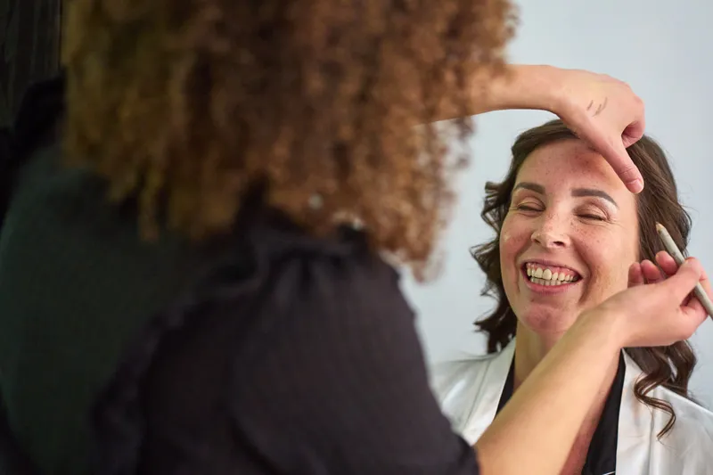 Michelle lacht met haar ogen dicht terwijl haar make-up wordt gedaan