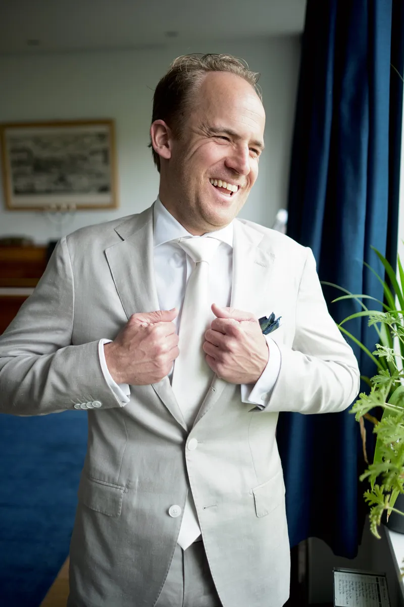 Jasper lacht in zijn lichte pak bij het raam