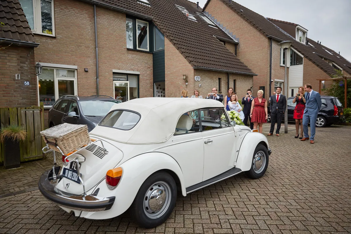 De witte Kever-cabrio staat voor het huis, de gasten wachten op straat