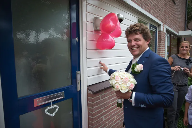 Matthijs staat met het boeket voor de deur, met roze hartjesballonnen