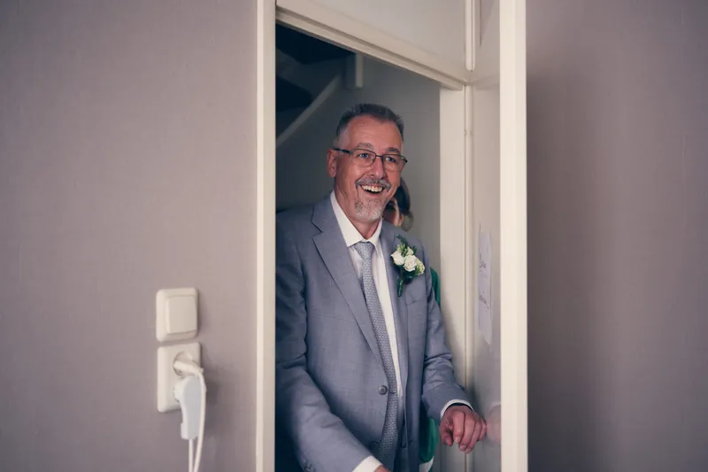 Marjolijns vader in de deuropening, met een bloem op zijn revers