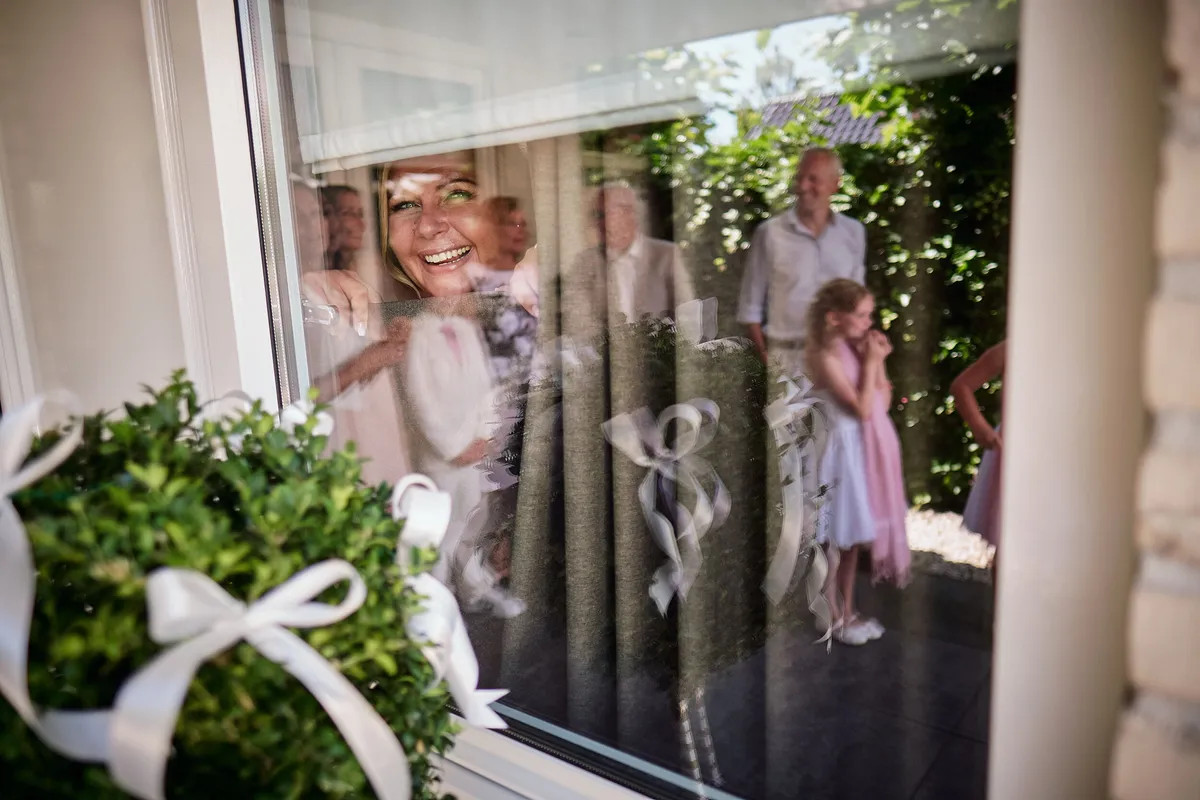 Vanessa lacht achter het raam, met bloemen op de voorgrond