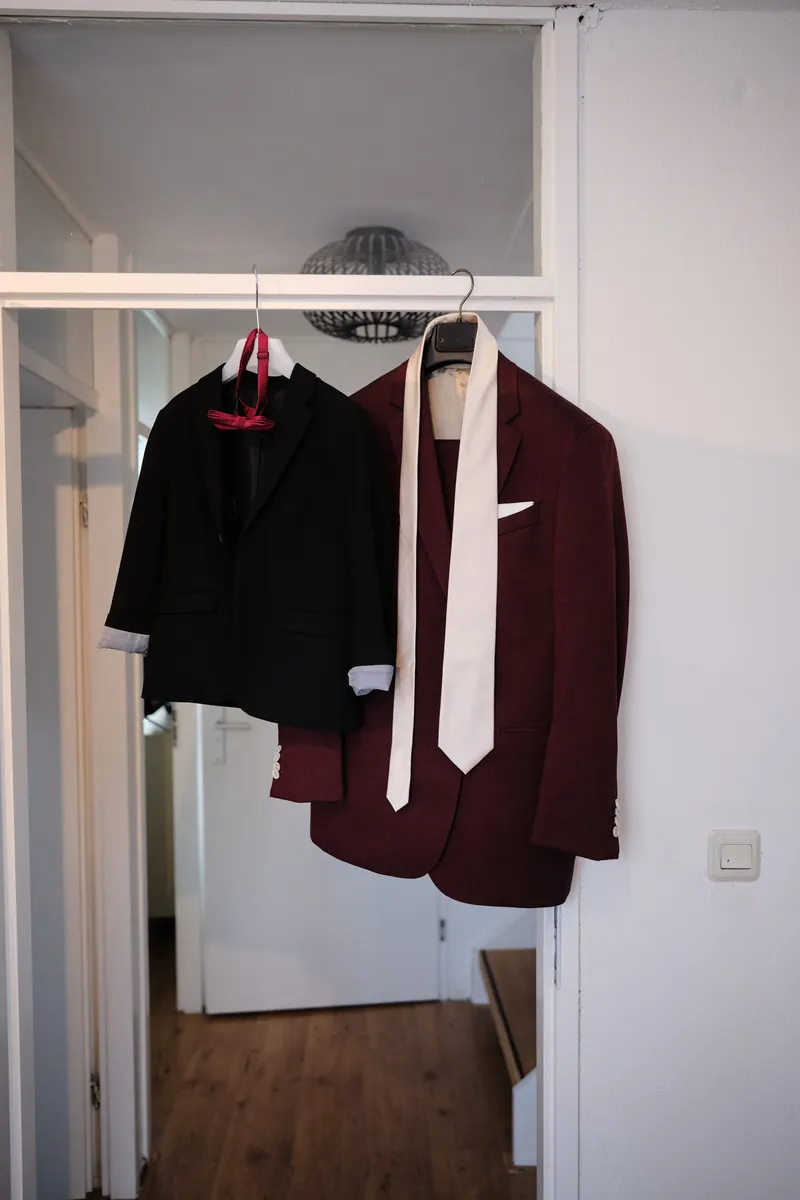 Het bordeauxrode pak van Tim en het pakje van zijn zoontje aan een hanger