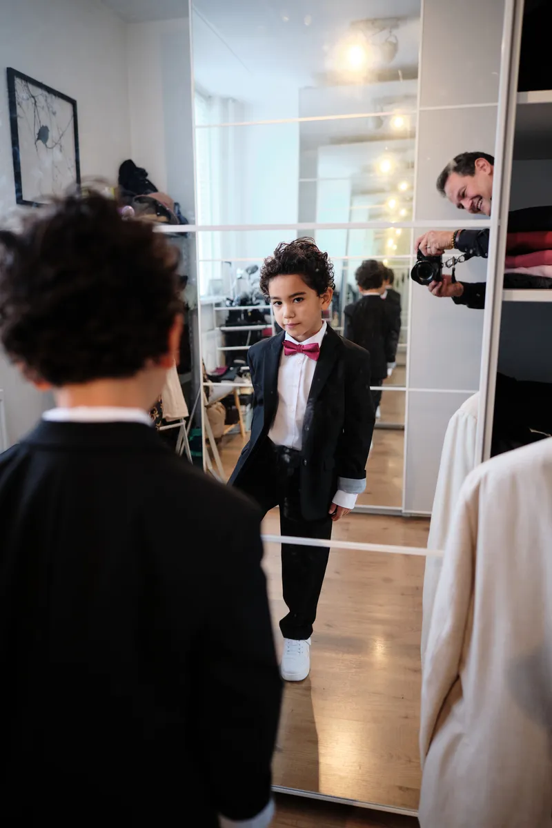 Het zoontje van Tim bekijkt zichzelf in de spiegel in zijn pakje met strikje