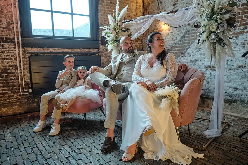 Regina en Michael op een roze bank voor de bakstenen muur, met hun zoon en dochter naast zich
