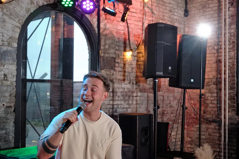 Gerrit Snijder zingt met de microfoon in de hand voor de hoge ramen