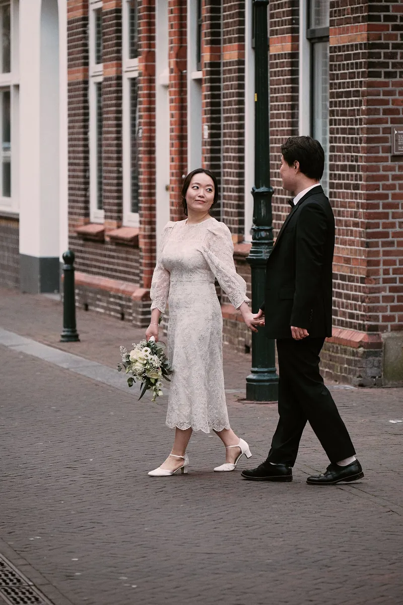 Een bruidspaar in trouwkleding loopt door een historisch straatje