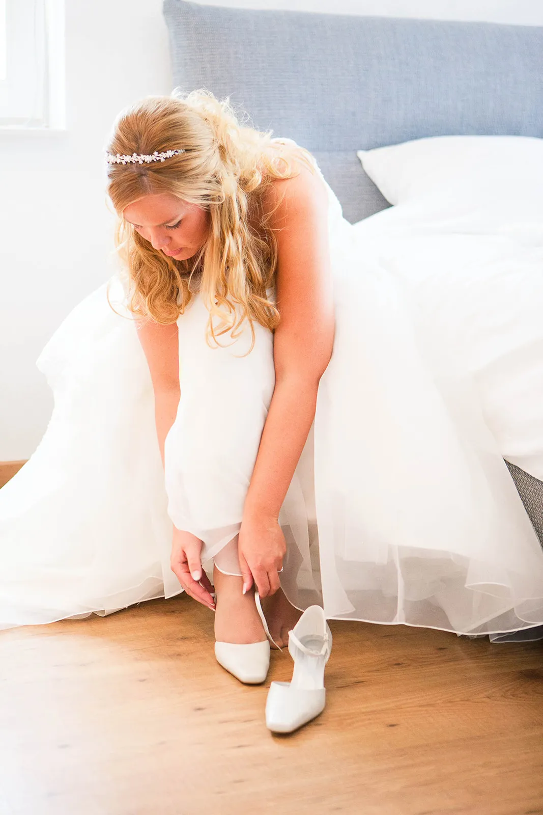 Bruid Esther trekt witte schoenen aan in slaapkamer voor bruiloft op Boerderij Dennisse