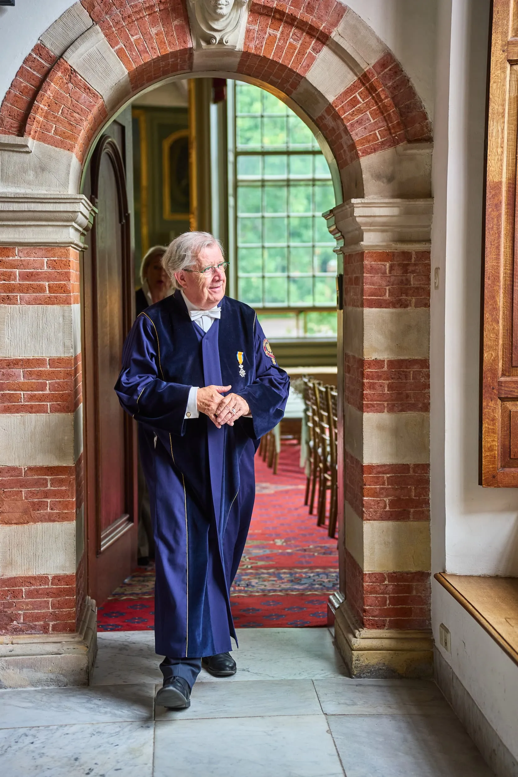 Bruidegom in donkerblauwe pak staat in klassieke bakstenen boog, trouwfotografie in elegant herenhuis — Trouwshoot Stefa
