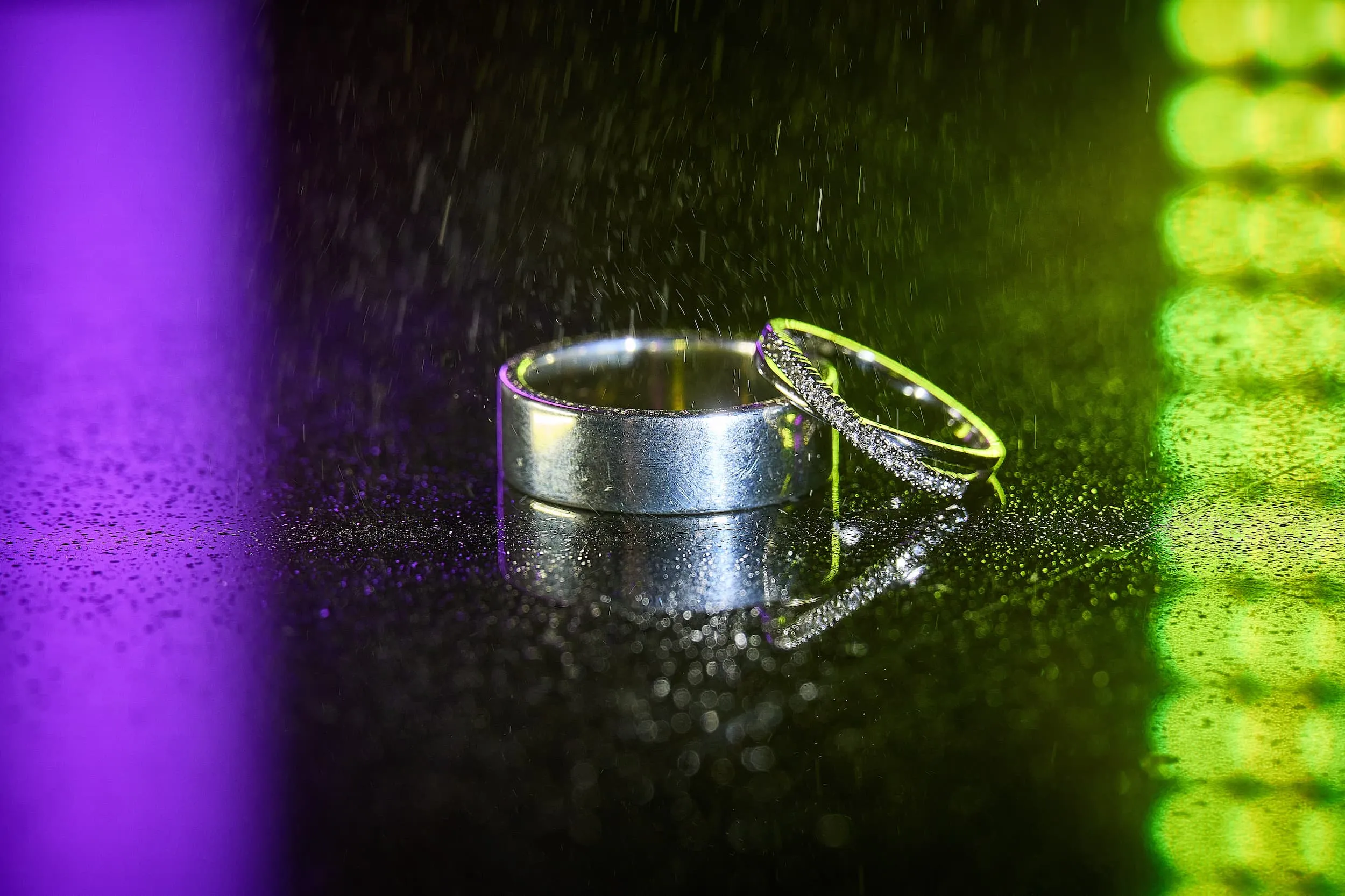 Twee trouwringen met diamanten op natte ondergrond, paars en groen licht, detailfotografie — Trouwshoot Stefan Segers