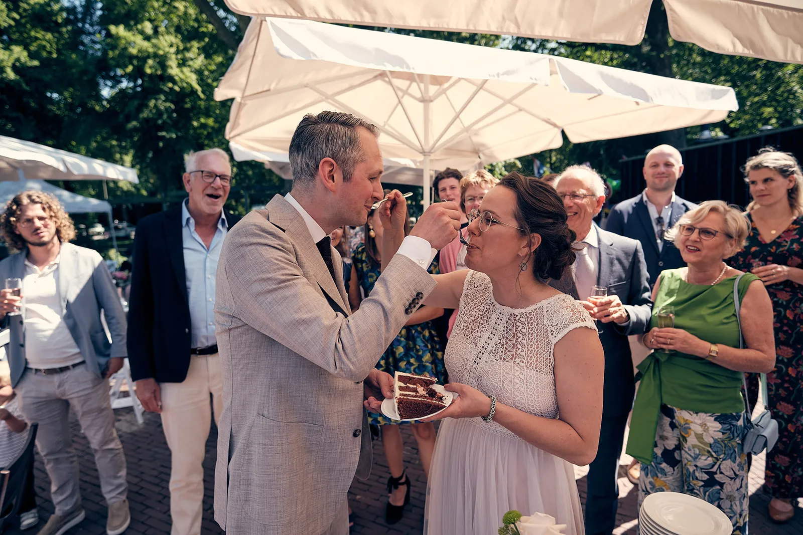 Bruidspaar Krijn en Evelien snijdt taart tijdens receptie onder parasols in De Schaapskooi Delft, trouwreportage
