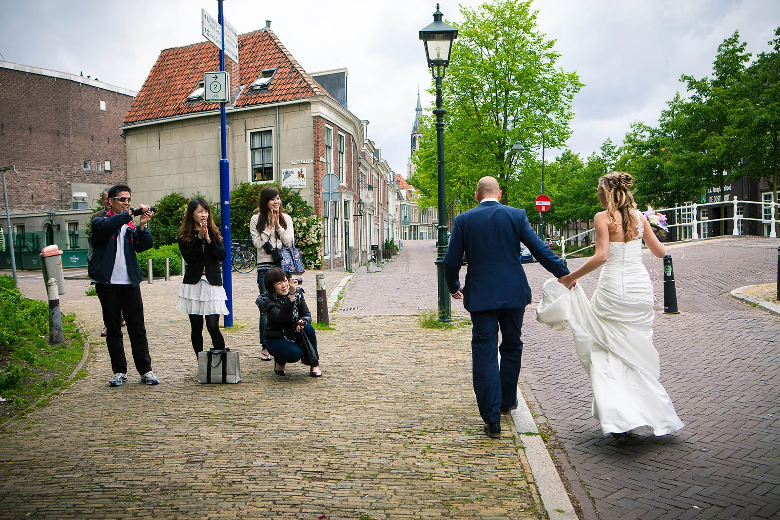 Bruidspaar Renate en Jesse loopt hand in hand door historische straat Delft, gasten fotograferen, trouwreportage