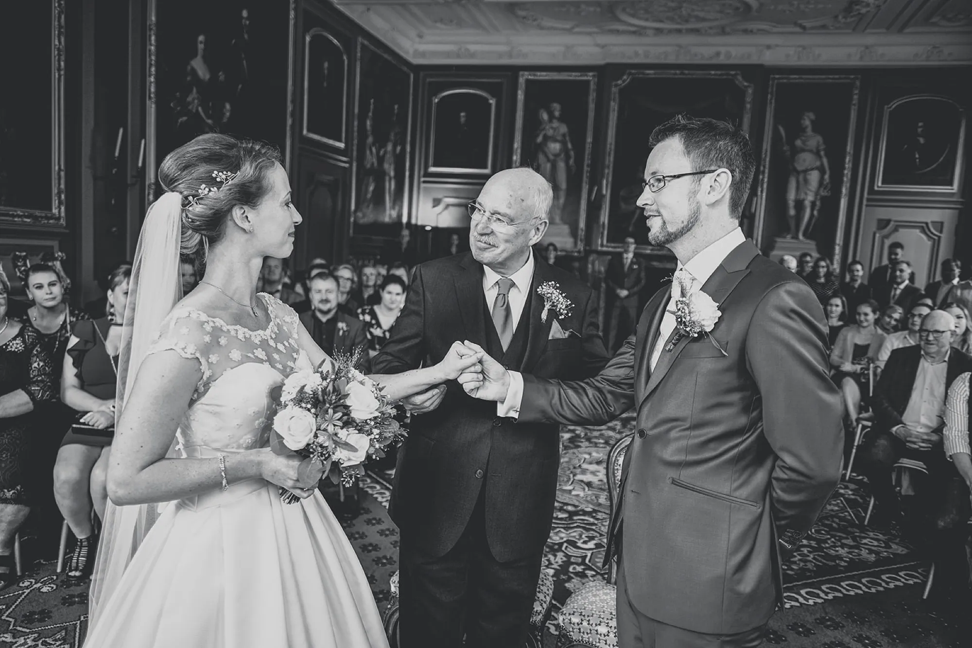 Vader geeft de hand van zijn dochter aan de bruidegom tijdens de ceremonie, zwart-wit