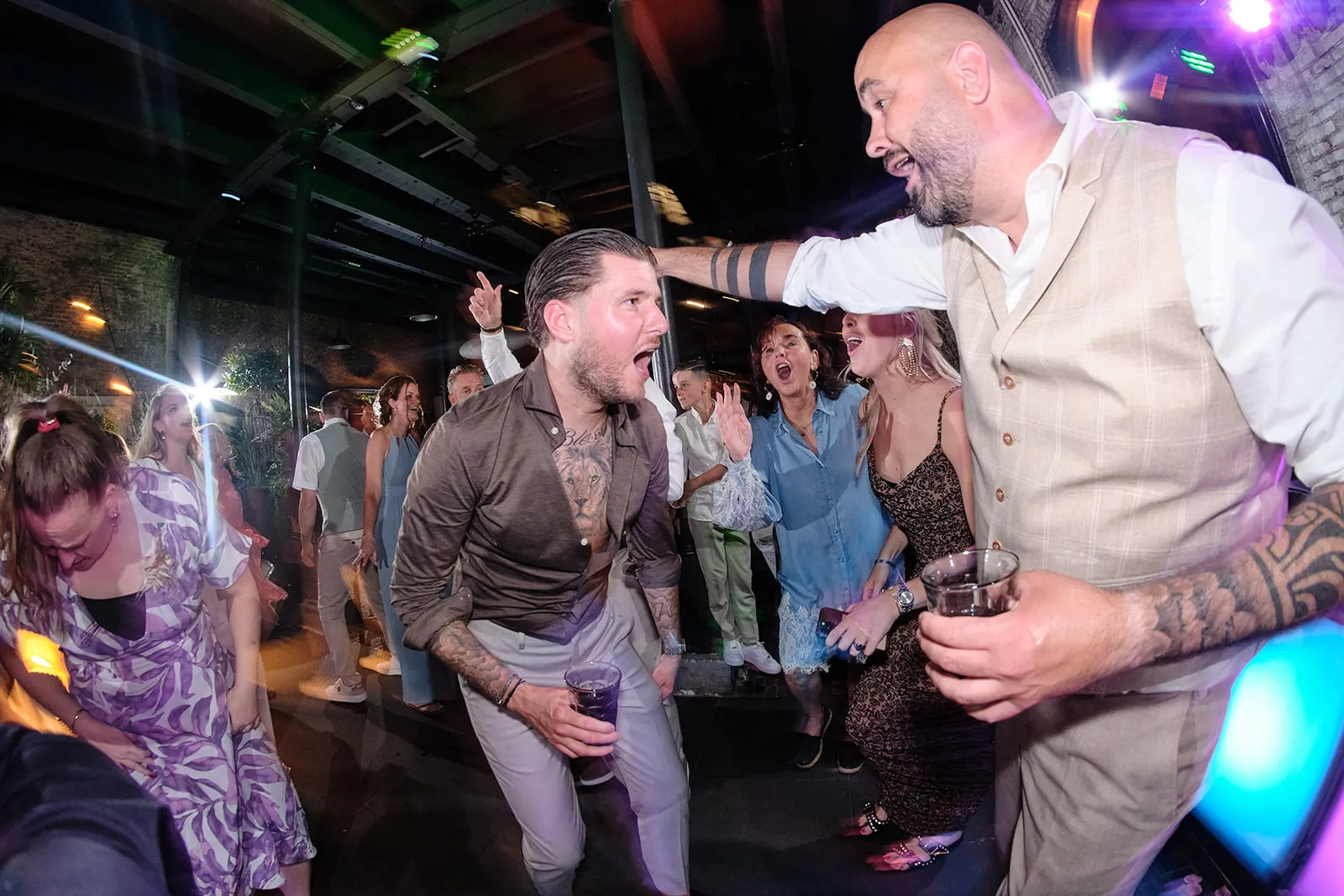 Bruidspaar en gasten dansen uitgelaten op trouwfeest Sodafabriek Schiedam, feestelijke trouwreportage met DJ en colorato lich