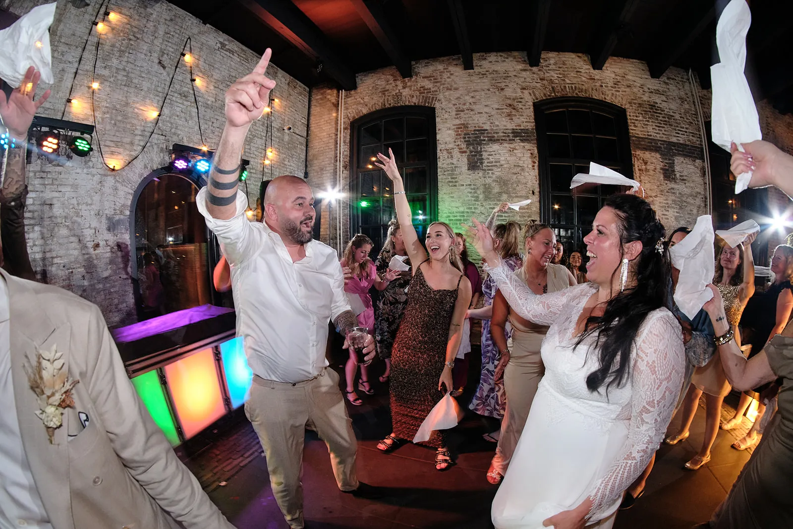 Bruidspaar danst uitbundig met gasten in Torpedoloods Schiedam, festive trouwreportage met neon verlichting