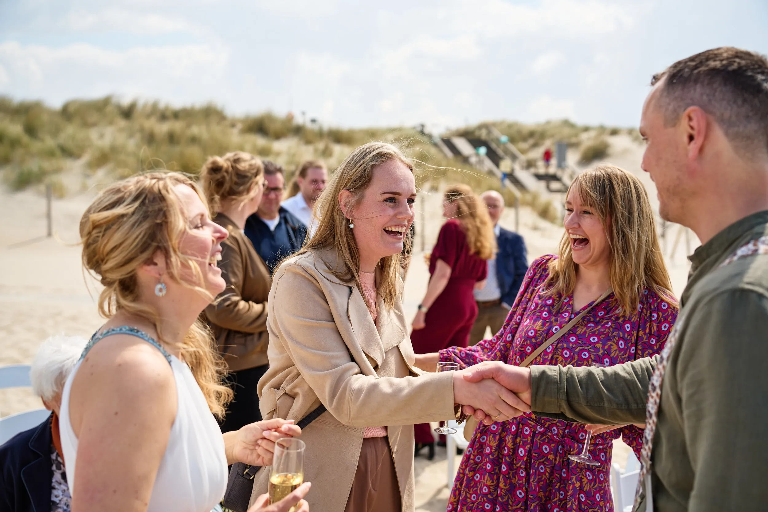 Tijdens de bruiloft van Elise en Erik bij Beachclub Titus in Kijkduin: bruid lachend met gasten op het strand