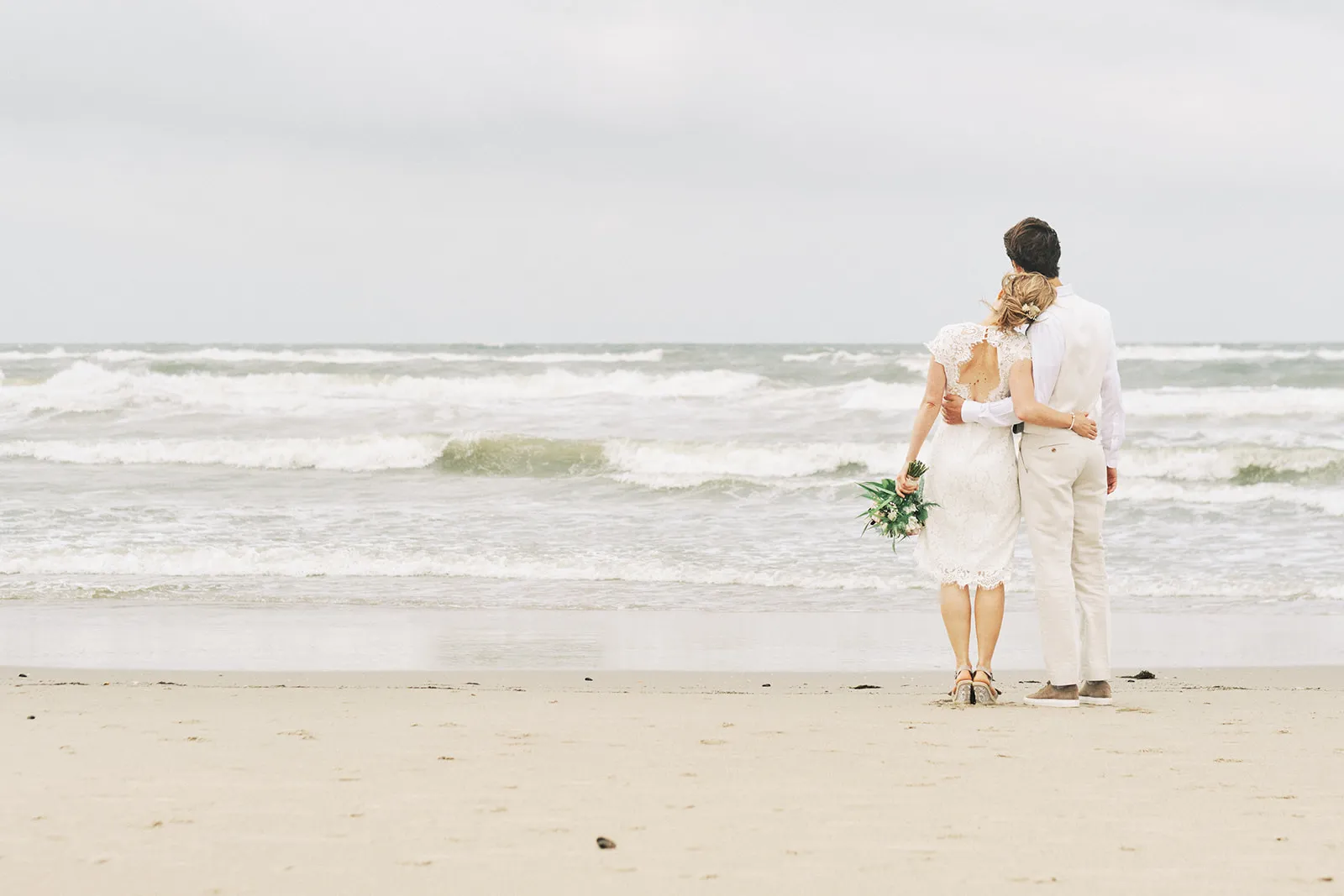 Bruidspaar Annemieke en Jaap op het strand van Kijkduin, verliefd moment in bruidsjurk en pak bij de zee, trouwreportage - Tr