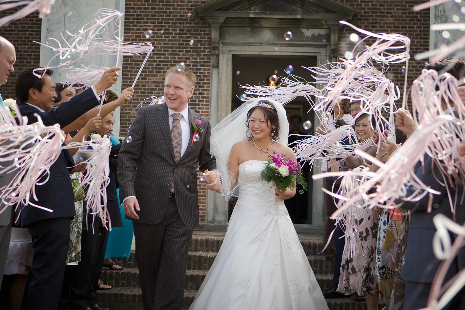 Bruidspaar Melissa en Michel verlaten kerk onder roze linten, trouwreportage Museum Hoffwijk Voorburg