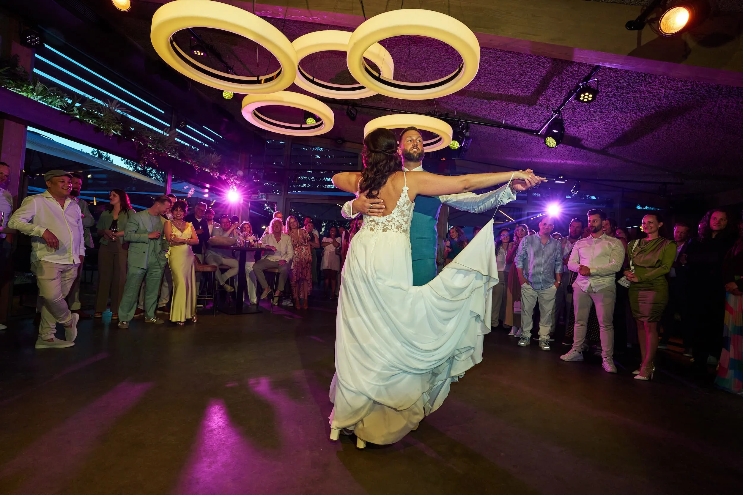 Bruidspaar danst uitbundig op trouwfeest in Rotterdam met paarse neonverlichting en neon ringen, feestfotografie — Trouw