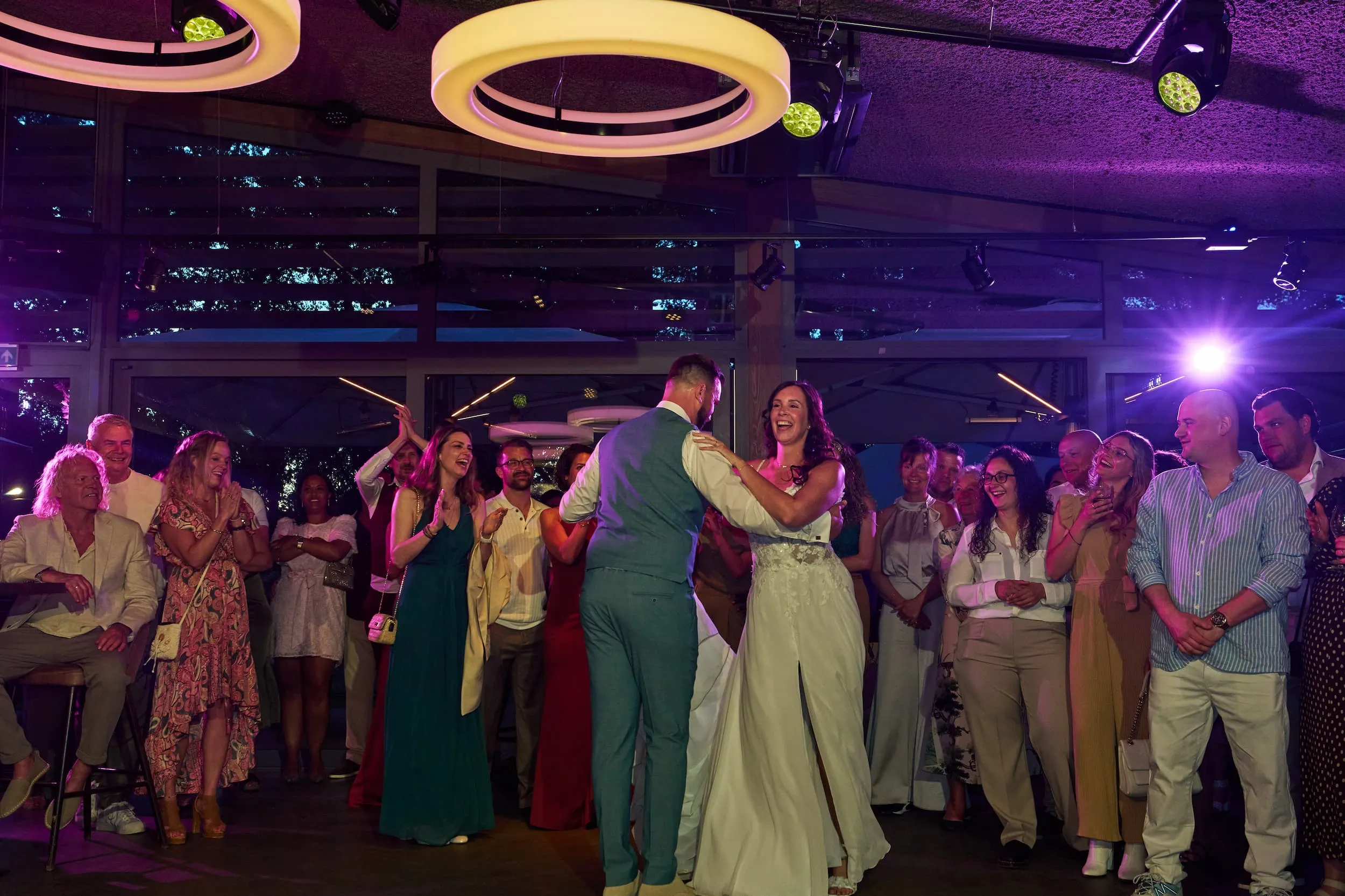 Bruidspaar danst tijdens trouwfeest in Rotterdam, gasten kijken toe onder paarse verlichting — Trouwshoot Stefan Segers