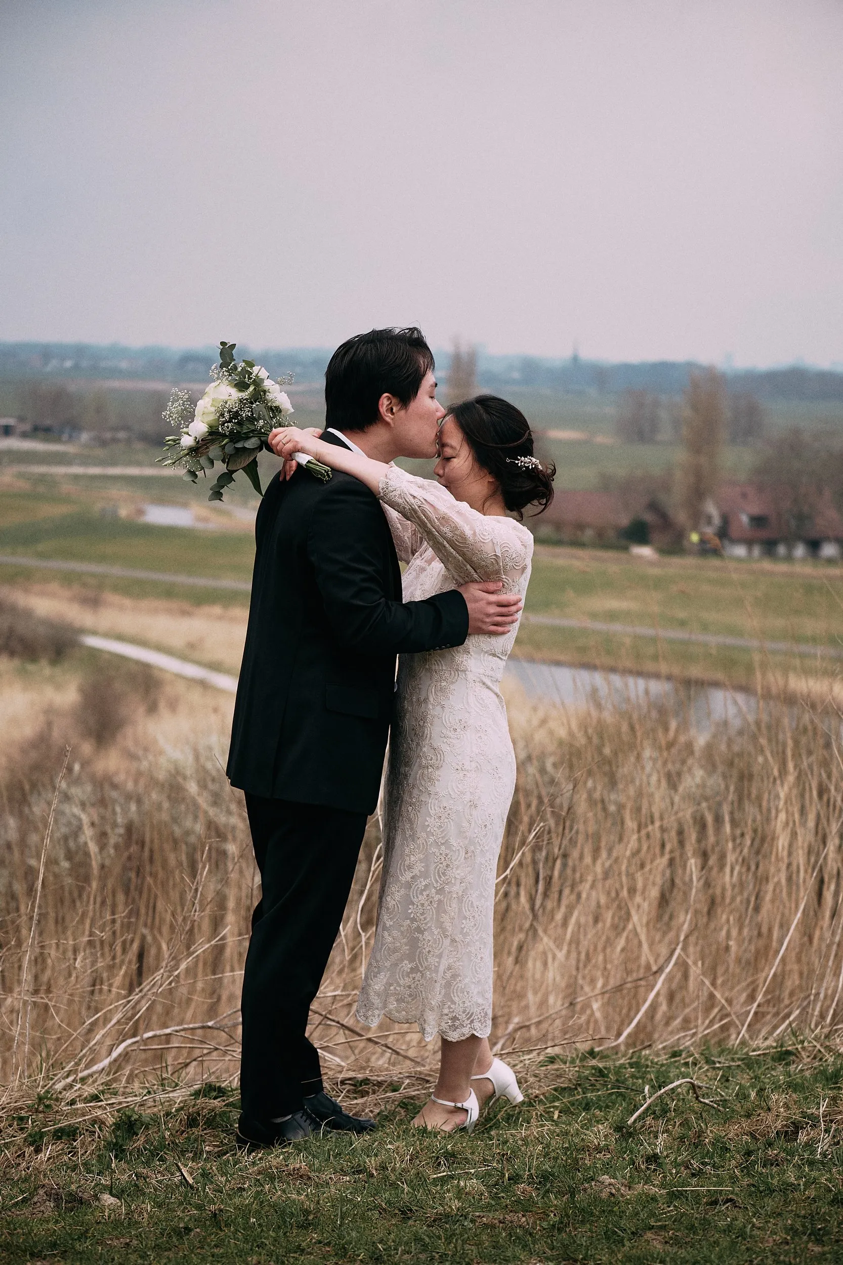 Verliefd bruidspaar omhelst elkaar in landelijk veld bij Zoetermeer, loveshoot met bruidboeket — Trouwshoot Stefan Seger