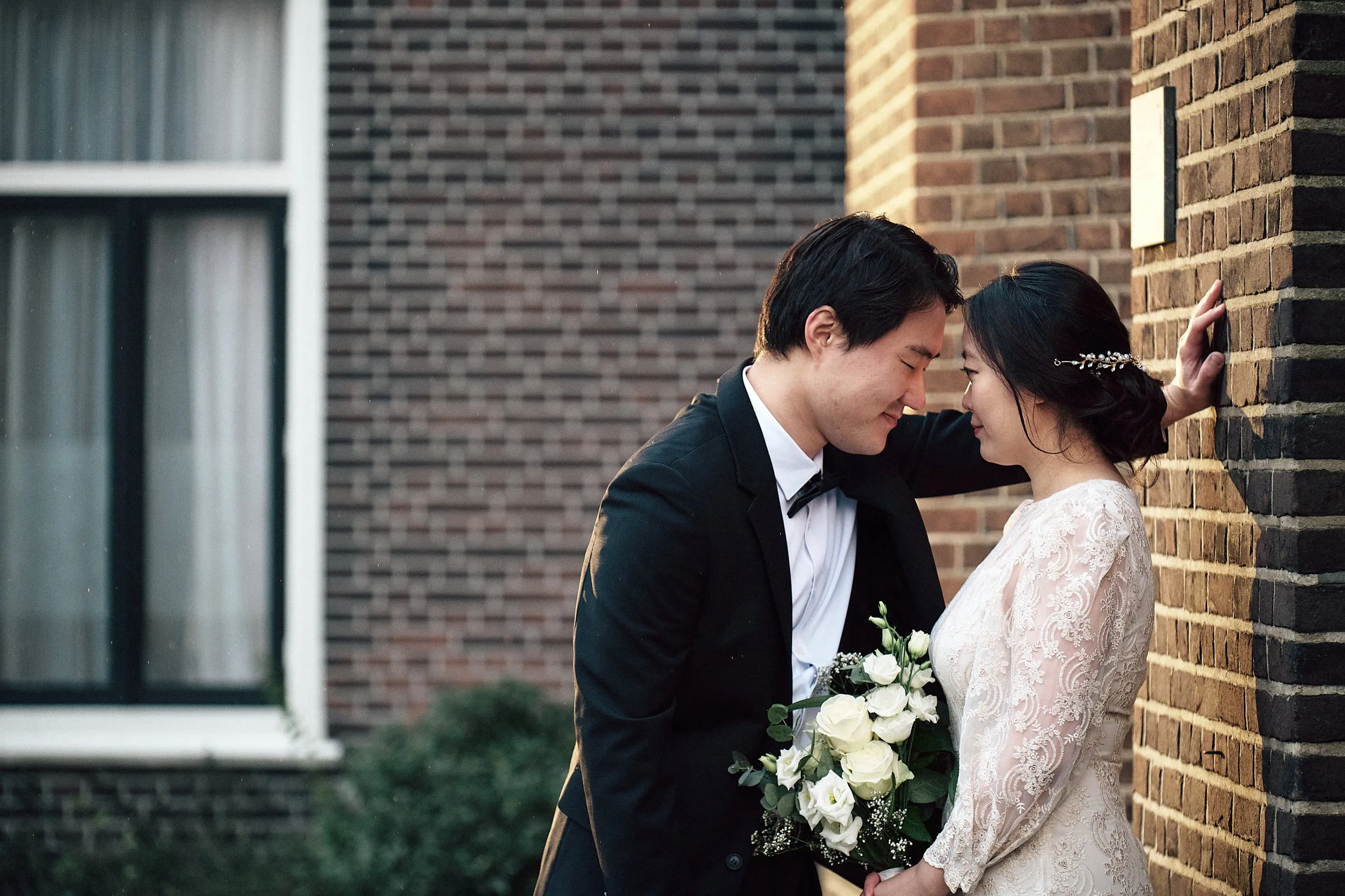 Verliefd bruidspaar staat zich aankijkend tegen bakstenen muur in Zoetermeer, loveshoot trouwfotografie — Trouwshoot Ste